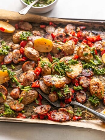 LIBAD Sheet Pan Sausage and Potatoes - cooked sheet pan with spatula, sausage, potatoes and peppers with chimichurri
