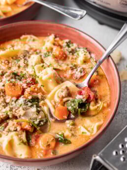 tortellini soup in a bowl with parmesan cheese and a spoon