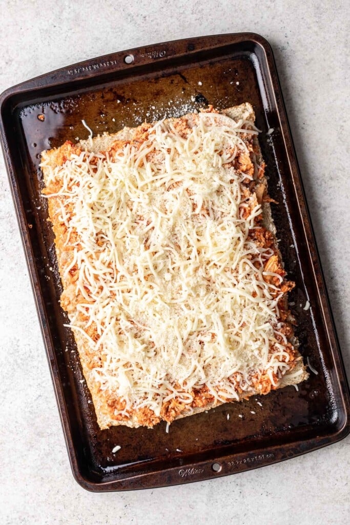 shredded chicken mixed with sauce on bread with shredded cheese on a sheet pan
