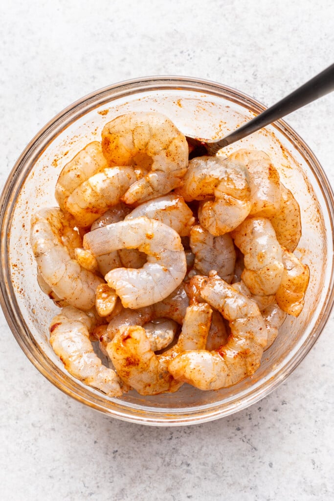 A bowl of raw shrimp with a spoon.