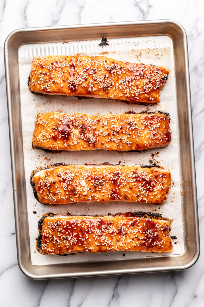 4 pieces of baked salmon on a baking sheet with bbq sauce and sesame seeds