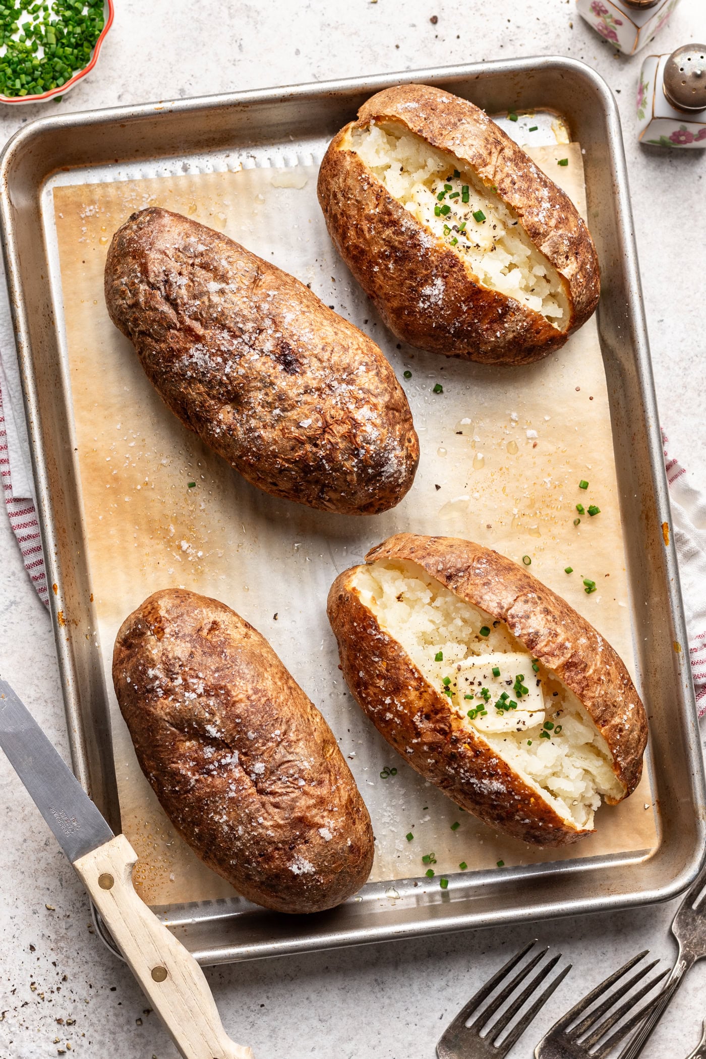 4 crispy baked potatoes on a sheet pan. Two are sliced open