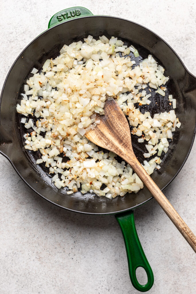 onions and garlic in a skillet with a wooden spoon