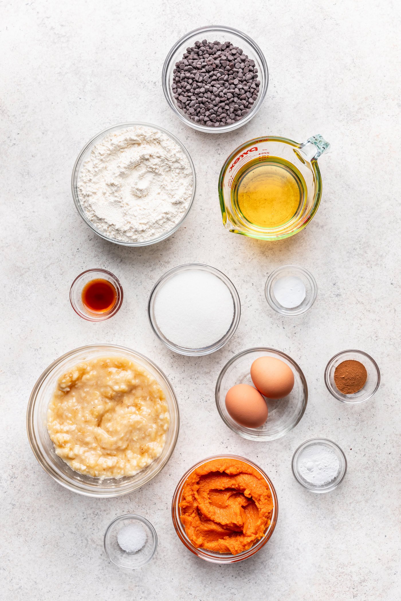 A flat lay of pumpkin puree, eggs, flour, chocolate chips, and spices for baking.