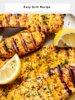 Grilled yogurt-marinated chicken breasts garnished with chopped herbs and lemon wedges on a plate. Text reads: Juicy Yogurt Marinated Chicken - Easy Grill Recipe.