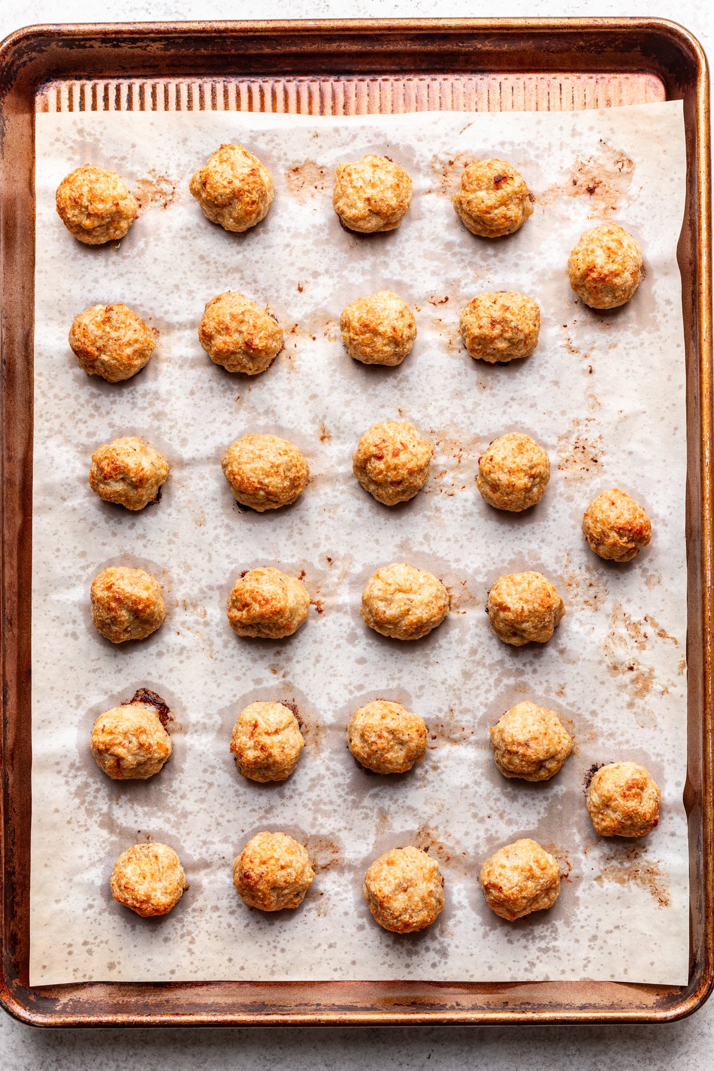 A baking sheet lined with parchment paper holds 28 evenly spaced, golden-brown sausage balls arranged in a grid pattern.