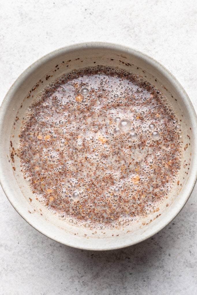 A ceramic bowl filled with a mixture of milk and chia seeds, creating a bubbly, slightly thick texture, on a light, textured surface.