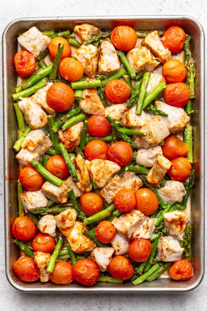 Sheet pan with chunks of cooked chicken, whole cherry tomatoes, and cut green beans, all seasoned and roasted, arranged evenly on a baking tray.