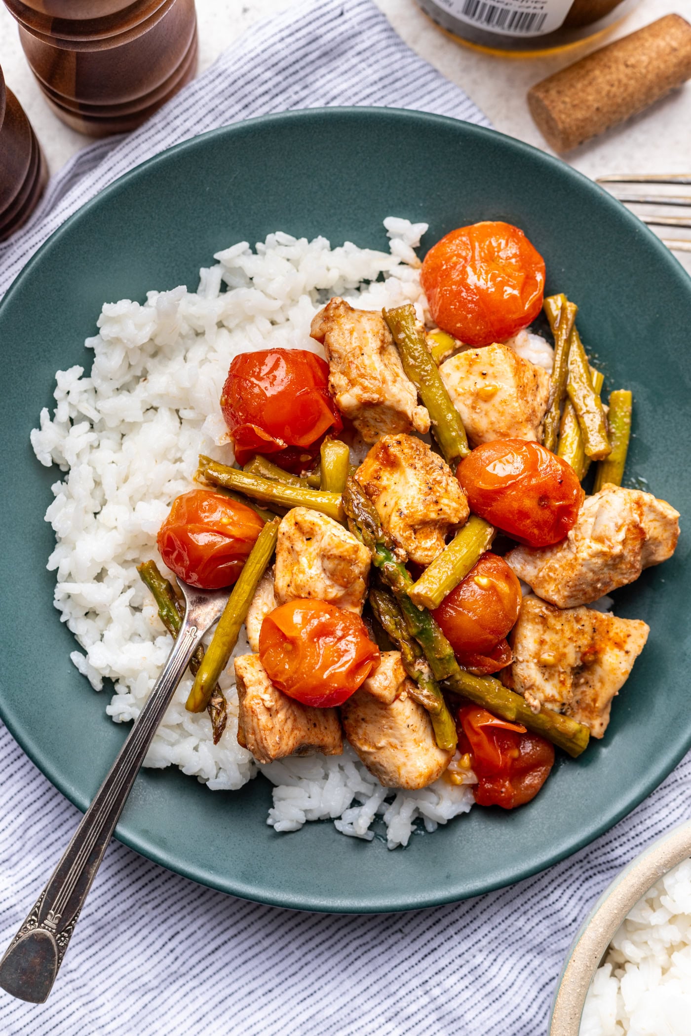 A plate of white rice topped with cooked chicken chunks, cherry tomatoes, and green beans, served with a fork on the side.