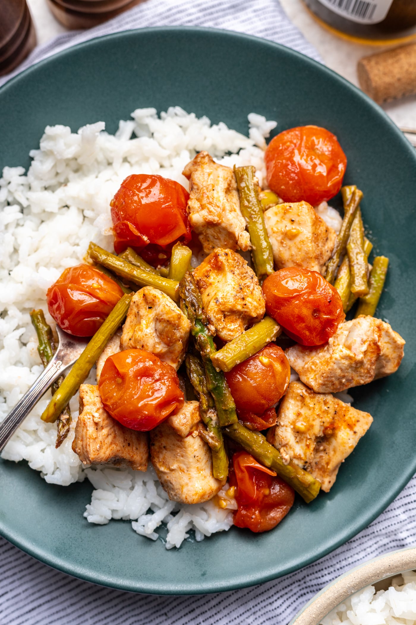 A green plate with white rice, grilled chicken pieces, cherry tomatoes, and green beans. A fork rests on the side of the plate. The meal looks fresh and colorful.