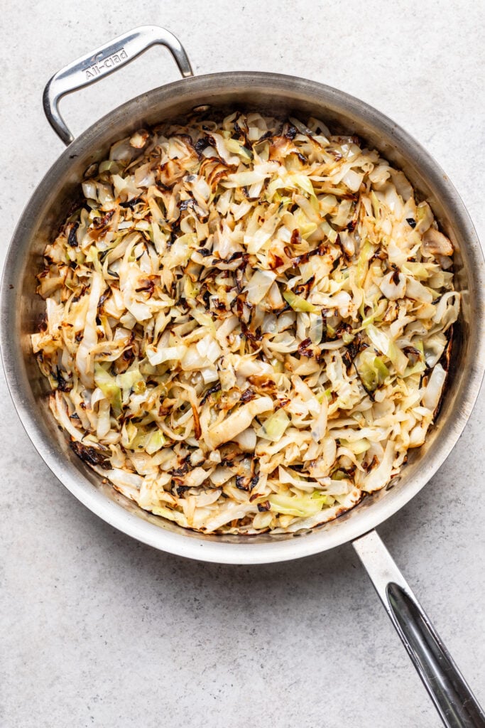 A stainless steel pan filled with sautéed, browned shredded cabbage sits on a light-colored countertop.
